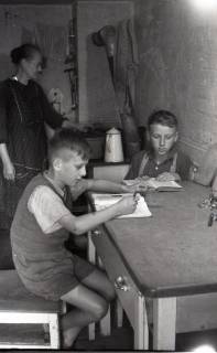 ARH NL Koberg 5013, Zwei lernende Kinder und eine kochende Frau in einem Keller in der Innenstadt, Hannover, 1945