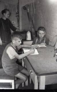 ARH NL Koberg 5014, Zwei lernende Kinder und eine kochende Frau in einem Keller in der Innenstadt, Hannover, 1945