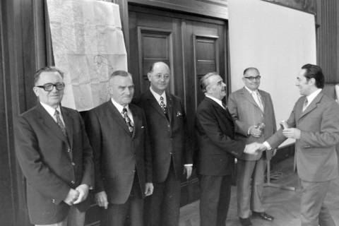 ARH NL Mellin 02-029/0009, Männer aufgereiht vor einer Wand stehend, zwei händeschüttelnd, ohne Datum