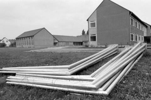 ARH NL Mellin 02-042/0015, Eisenrohre auf dem Rasen vor einem Schulgebäude mit Sporthalle (?), ohne Datum