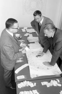 ARH NL Mellin 02-077/0005, Drei Männer um einen Tisch mit einem Plan des Kuppelsaals des Hannover Congress Centrums (HCC) stehend, ohne Datum