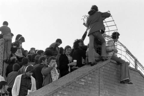 ARH NL Mellin 02-081/0014, Fußballfans auf den Mauern neben den Zuschauertribünen eines Fußballstadions ?, ohne Datum
