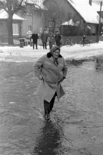 ARH NL Mellin 02-101/0016, Eine Frau beim Durchqueren einer überschwemmten Straße im Winter, ohne Datum