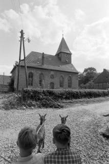 ARH NL Mellin 02-126/0004, Blick über zwei Jungen in einem Wagen mit zwei vorgespannten Ziegen hinweg auf die St. Georg Kirche, Holtensen, vor 1969
