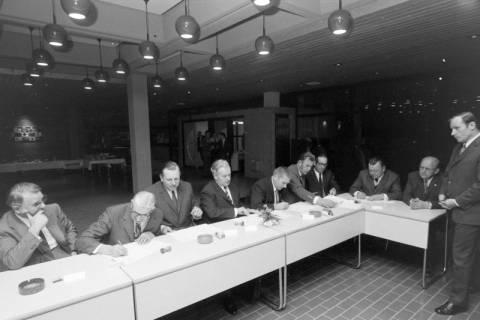 ARH NL Mellin 02-132/0010, Männer beim Unterzeichnen von Unterlagen an einer Tischreihe sitzend, um 1975