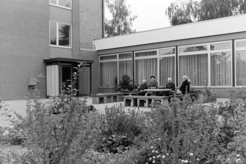 ARH NL Mellin 02-162/0004, Gruppe von älteren Damen auf Bänken vor einem Gebäude sitzend, um 1975
