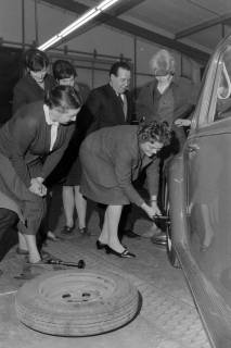 ARH NL Mellin 02-173/0006, Frau beim Radwechsel an einem Auto vor einem Publikum, um 1975