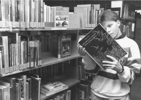 ARH Slg. Bartling 379, Jugendlicher vor einem Bücheregal stehend und in ein aufgeschlagenes Buch über Blütengärten schauend, Neustadt a. Rbge., um 1970