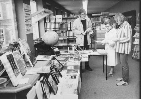 ARH Slg. Bartling 381, Kleine Buchausstellung mit auf Tischen ausgelegten Büchern über Niedersachsen mit drei interessierten Lesern, um 1970