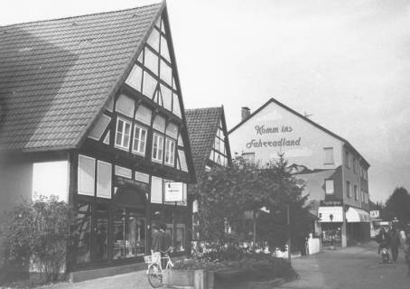ARH Slg. Bartling 768, Windmühlenstraße 17-20, Blick nach Norden Fahrrad Plinke (Giebelwand mit Werbung "Komm ins Fahrradland"), Geschäftsstelle der Leine-Zeitung (Schrägansicht des Giebels von Südosten), Neustadt a. Rbge., um 1980