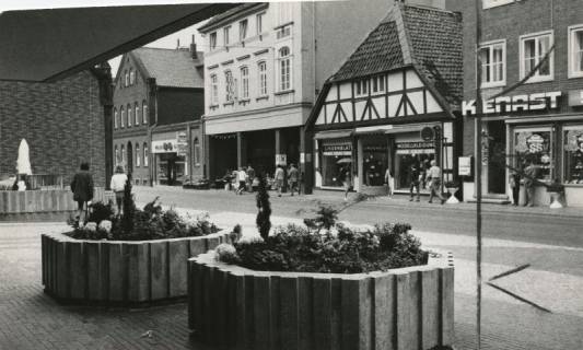 ARH Slg. Bartling 997, Marktstraße 10-11, Modellkleidung Lindenblatt, Giebelwand des Fachwerkbaus mit gekrücktem Dach Blick vom Vorplatz der neuen Kreissparkasse über die Blumenkübel auf die nördliche Straßenseite, Neustadt a. Rbge., 1972