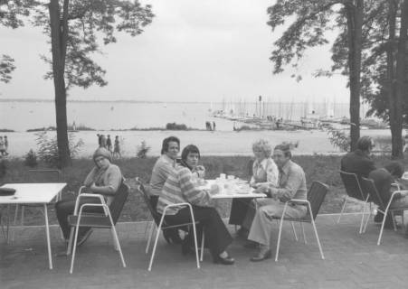 ARH Slg. Bartling 1217, Nordufer, Blick auf eine Gruppe von Gästen auf der Terrasse des Restaurants Weisse Düne, dahinter der Uferweg, der leere Badestrand und der See mit Bootssteg (rechts), Steinhuder Meer, um 1970