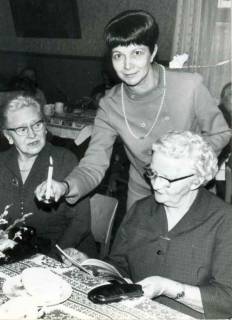 ARH Slg. Bartling 1375, Ilse Krautter (Vorsitzende des Vorstands des DRK) reicht bei einer Versammlung des Altenclubs des DRK im Gasthaus Küster zwei Teilnehmerinnen eine brennende Weihnachtsbaumkerze, Mandelsloh, um 1970