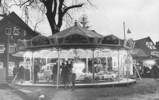 ARH Slg. Bartling 1487, Beleuchtetes Kinderkarussell auf dem Kirchplatz unter der Kastanie in der Dämmerung, Neustadt a. Rbge, 1974