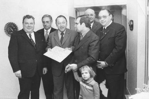 ARH Slg. Bartling 1668, Der Niedersächsische Wirtschaftsminister Helmut Greulich (3. v. l.)  zeigt dem Betrachter ein flaches Geschenk, Neustadt a. Rbge., um 1970
