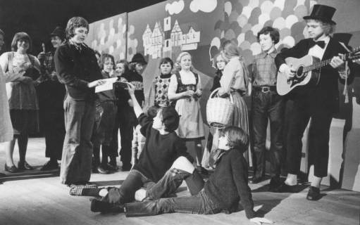 ARH Slg. Bartling 1737, Schüler spielen Theater, rechts ein Gitarrist mit Zylinder; als Kulisse dient eine Wand mit stilisierter Darstellung einer Stadtansicht und bunten Luftballons, Neustadt a. Rbge., 1974