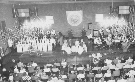ARH Slg. Bartling 1775, Weihnachtsfeier im Saal des Freizeitzentrums, auf der Bühne in der Mitte eine Diskussionsgruppe von sechs Personen am runden Tisch, links davon eine Combo, rechts ein Akkordeonorchester, Neustadt a. Rge., um 1975