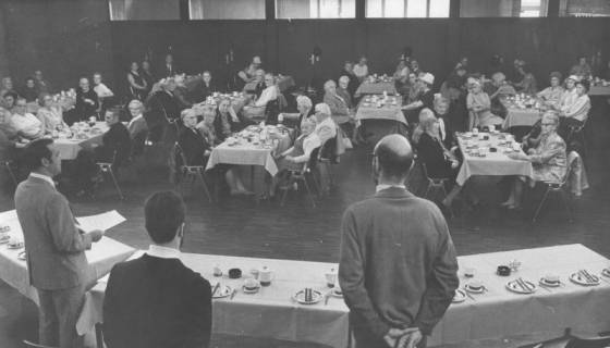 ARH Slg. Bartling 1885, Senioren und Seniorinnen an einer Kaffeetafel im Freizeitzentrum, davor an quer gestellten Tischen mit dem Rücken zum Betrachter stehend drei Männer (links Ratsherr Wolfgang Kirchmann), Neustadt a. Rbge., 1972