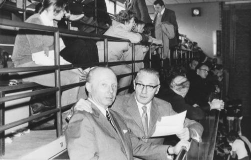 ARH Slg. Bartling 2097, Zwei ältere Männer mit anderen Zuschauern sitzend auf der Tribüne einer Turnhalle, Blick von rechts auf die erste Reihe, um 1975
