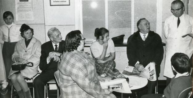 ARH Slg. Bartling 2323, Patienten im überfüllten Warteraum des Gesundheitsamtes sitzend, Dr. Simon Kaindl (r.) stehend und den wartenden Patienten zuhörend, Neustadt a. Rbge., 1971