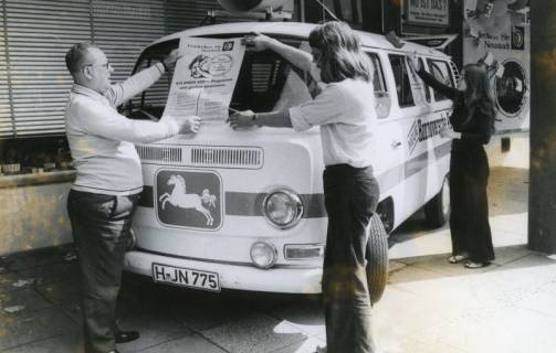 ARH Slg. Bartling 2542, Anbringung eines Werbeplakats an der Frontscheibe eines VW-Bullis der Neuen Hannoverschen Presse (NHP), vor der Geschäftsstelle der NHP, Marktstaße 12, Neustadt a. Rbge., 1972