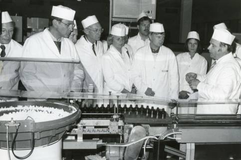 ARH Slg. Bartling 2571, Firma Kali-Chemie-AG, Arzneimittelwerk Neustadt, Suttorfer Straße 1, Besuchergruppe in weißer Schutzkleidung hinter einer Abfüll-Fließbandanlage, Neustadt a. Rbge., um 1970