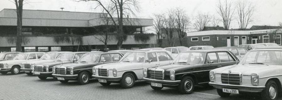 ARH Slg. Bartling 2641, Tagung der Oberkreisdirektoren im FZZ, auf dem Parkplatz vor dem FZZ-Gebäude in Reih und Glied nebeneinander abgestellte Dienstwagen (Mercedes 200D/8), rechts der Bungalow des Schützenhauses, Neustadt a. Rbge., um 1975