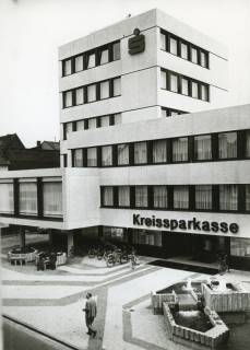 ARH Slg. Bartling 2703, Neubau der Kreissparkasse an der Marktstraße, Blick vom Giebel des Hauses Marktstraße 11a auf den Eingangsbereich des Gebäudes samt Turm und Brunnenanlage, Neustadt a. Rbge., 1973
