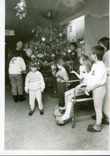 ARH Slg. Bartling 3176, Kreiskrankenhaus (später: KRH Klinikum Neustadt a. Rbge.), Lindenstraße 75: Aufstellung eines geschmückten Weihnachtsbaums auf dem Flur der Kinderstation durch das DRK - Ortsgruppe Bordenau unter den Augen von sechs Kindern im Vordergrund, Neustadt a. Rbg, um 1973