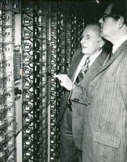 ARH Slg. Bartling 3183, Besichtigung einer elektromechanischen Vermittlungsstelle durch zwei davor stehende Beamte beim Postamt, Neustadt a. Rbge., , um 1971