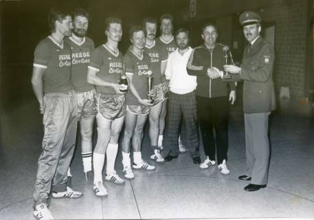 ARH Slg. Bartling 3379, Überreichung eines zweiten Pokals an ein Handballteam (in Spielerhemden mit Werbeaufdruck der Firma Reese Öl+Gas) in einer Sporthalle durch einen Polizisten, Neustadt a. Rbge., um 1974