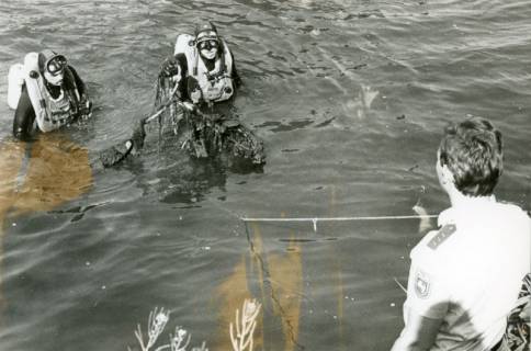 ARH Slg. Bartling 3409, Entgegennahme eines völlig verschmutzten von zwei Polizeitauchern in der Leine gefundenen und aus dem Wasser gehaltenen Fahrrades durch einen am Ufer stehenden Polizisten, Neustadt a. Rbge., 1974