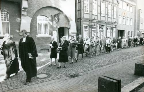 ARH Slg. Bartling 3529, Prozession einer großen Zahl von Frauen auf der Schulstraße von der Marktstraße zum Haupteingang der Liebfrauenkirche, angeführt von zwei Pastoren im Talar, Neustadt a. Rbge., um 1974