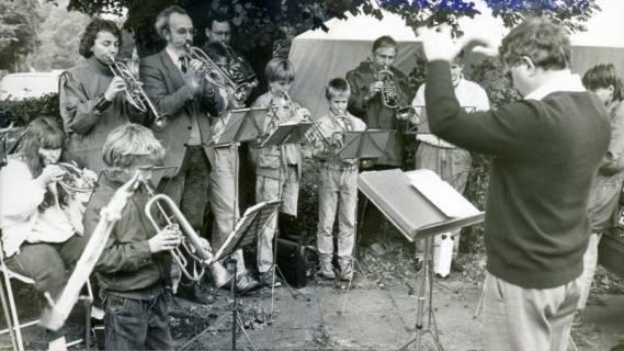 ARH Slg. Bartling 3556, Gruppenbild einer gemischten Blaskapelle (mit Erwachsenen und Kindern) unter einem Laubbaum vor einem Mannschaftszelt, um 1985