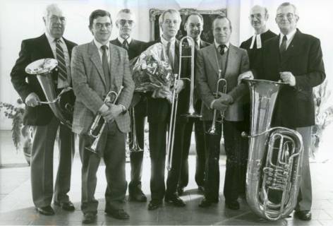 ARH Slg. Bartling 3557, Gruppenbild einer mit einem Blumenstrauß geehrten Blaskapelle von sieben Männern mitsamt Pastor N. N. im Talar vor dem Kanzelaltar der Evangelisch-lutherischen Kirche, Helstorf, 1985