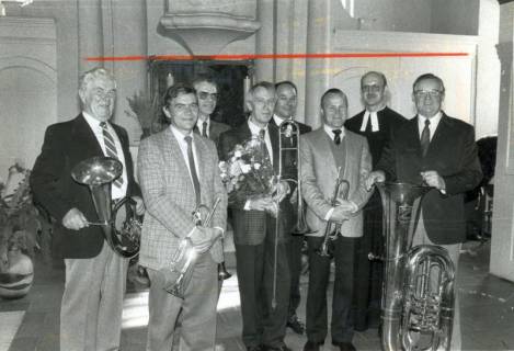 ARH Slg. Bartling 3558, Gruppenbild einer mit einem Blumenstrauß geehrten Blaskapelle von sieben Männern mitsamt Pastor N. N. im Talar vor dem Kanzelaltar der Evangelisch-lutherischen Kirche, Helstorf, um 1985
