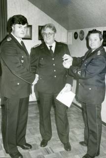 ARH Slg. Bartling 3681, Ehrung von Eduard Formella durch Überreichung einer Urkunde und eines Anhängers in einem Dachzimmer durch Stadtbrandmeister Horst Liem (r.) und Ortsbrandmeister Heinrich Lammers (l.) im Gerätehaus, An der Beeke, Mariensee, um 1985