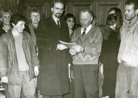ARH Slg. Bartling 3737, Überreichung einer Akte an N. N. durch N. N. im Beisein von mehreren jüngeren Leuten vor einer Wand mit Verkleidung aus Holzkassetten, Neustadt a. Rbge., 1989
