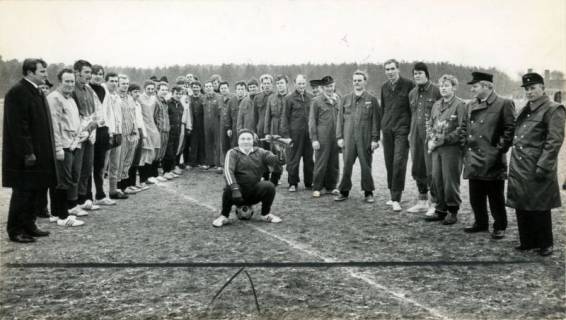 ARH Slg. Bartling 3795, Gruppenfoto der beiden Fußballmannschaften der Feuerwehr (in Arbeitsuniform) - TSV Poggenhagen, in der Mitte auf einem Ball sitzend Schiedsrichter Willi Lottich mit einem Feuerhorn, Poggenhagen, 1971