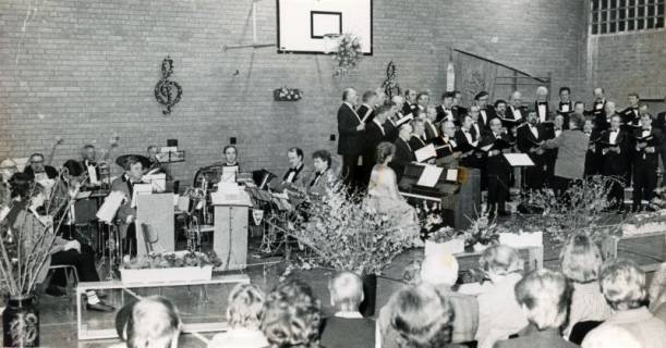 ARH Slg. Bartling 3936, "Singendes, klingendes Bordenau" in der Turnhalle, Auftritt des Männergesangvereins unter dem Dirigat von Gerhard Bruns, links daneben die Bordenauer Blaskapelle auf der Bühne, Bordenau, 1989