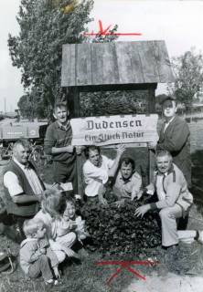 ARH Slg. Bartling 3987, "Dudensen. Ein Stück Natur." Ortseingangsschild, gestaltet im Rahmen des Wettbewerbs "Unser Dorf soll schöner werden". Eine Gruppe mit Familie posiert am Schild, Dudensen, um 1975