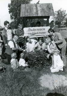 ARH Slg. Bartling 3988, "Dudensen. Ein Stück Natur." Ortseingangsschild, gestaltet im Rahmen des Wettbewerbs "Unser Dorf soll schöner werden". Eine Gruppe mit Familie posiert am Schild, Dudensen, um 1975