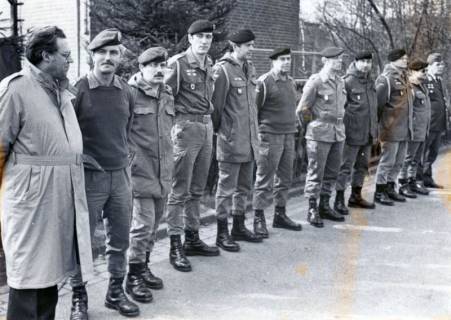 ARH Slg. Bartling 4325, Gruppe von 11 nebeneinander stehenden älteren Soldaten in unterschiedlichen Uniformen vor Kasernengebäude, links ein Soldat (?) in Zivil, Luttmersen, um 1985