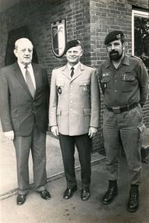 ARH Slg. Bartling 4334, Gruppenporträt der drei Männer Herbert Schöling (in Zivil), Schmelzer (in Dienstuniform) und Kompaniechef Busch (in Arbeitsuniform, mit Vollbart) vor einem Kasernengebäude mit Wappenschild, Luttmersen, um 1985