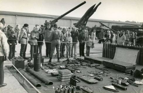 ARH Slg. Bartling 4384, Tag der offenen Tür, Ausstellung der Bordausrüstung eines Panzers auf dem Vorplatz der Panzer-Hallen , Blick über die auf dem Boden ausgelegten Gegenstände auf die vor den Hallen stehenden schweren Geschütze, Luttmersen, um 1975