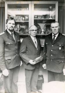 ARH Slg. Bartling 4431, Ehrung von drei Feuerwehrleuten, stehend vor einer mit Pokalen und Tellern gefüllten Vitrine, v. l. n. r.: Ortsbrandmeister Heinz Nebel, N.N., W. Oehlerking, Mandelsloh, um 1980