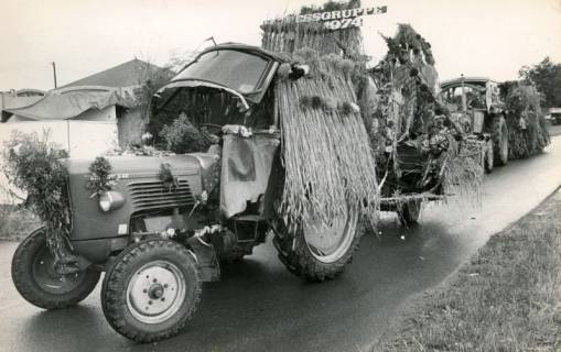 ARH Slg. Bartling 4491, Zwei Trecker auf der Straße die mit Blumen und Stroh geschmückt sind beim Erntefestumzug, Mariensee, 1974