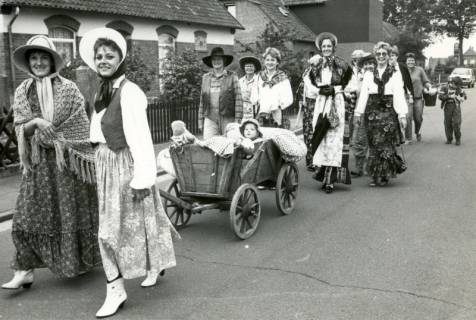 ARH Slg. Bartling 4492, Junge Frauen in "historischen" Kleidern ziehen einen Bollerwagen mit einem Kind durch die Straßen beim Erntefestumzug, Mariensee, um 1975