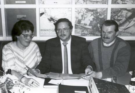 ARH Slg. Bartling 4530, Helga Rübenhaus, Christian Herr (Pächter des Restaurants Weiße Düne und Vorsitzender des Verkehrsvereins Mardorf) und Karl Syrup nebeneinander am Tisch vor einer Wand mit topografischen Karten in der Sprechstelle der Stadt Neustadt sitzend, Mardorf, um 1980