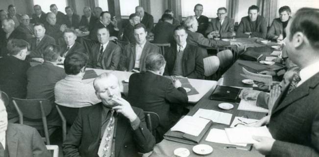 ARH Slg. Bartling 4765, Versammlung der Otternhagener Landwirte, die an langen Tischen sitzen, rechts der quer gestellte Vorstandstisch mit dem stehenden Redner, Otternhagen, 1972